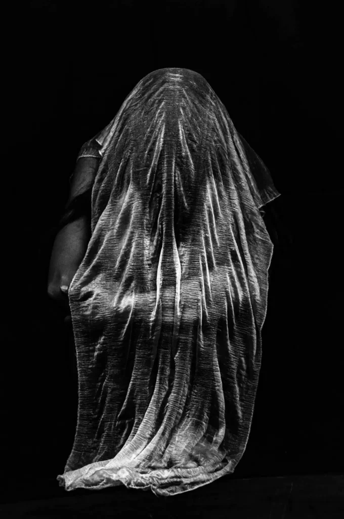 Silhouette humaine recouverte d’un voile, photographie artistique en noir et blanc.