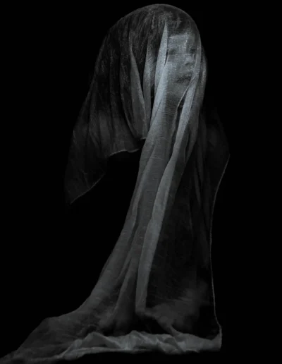 Silhouette voilée en noir et blanc, drap flottant dans l’obscurité.